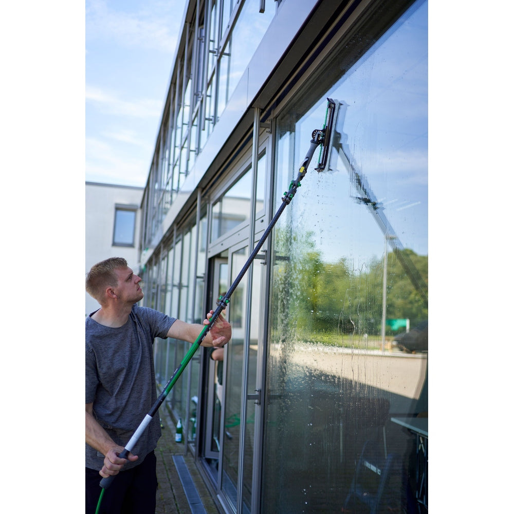 Person reinigt Fenster eines Gebäudes mit UNGER Reinwasser Set und nLITE PowerPad.